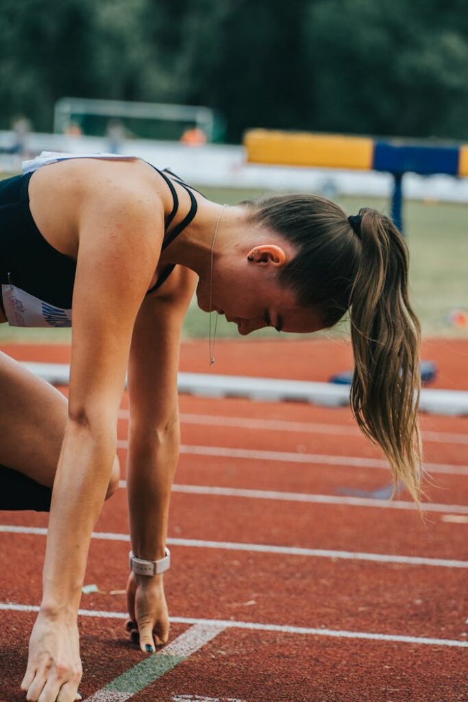 pexels-photo-8820688 Focused female athlete on starting line of a track, ready to sprint outdoors.